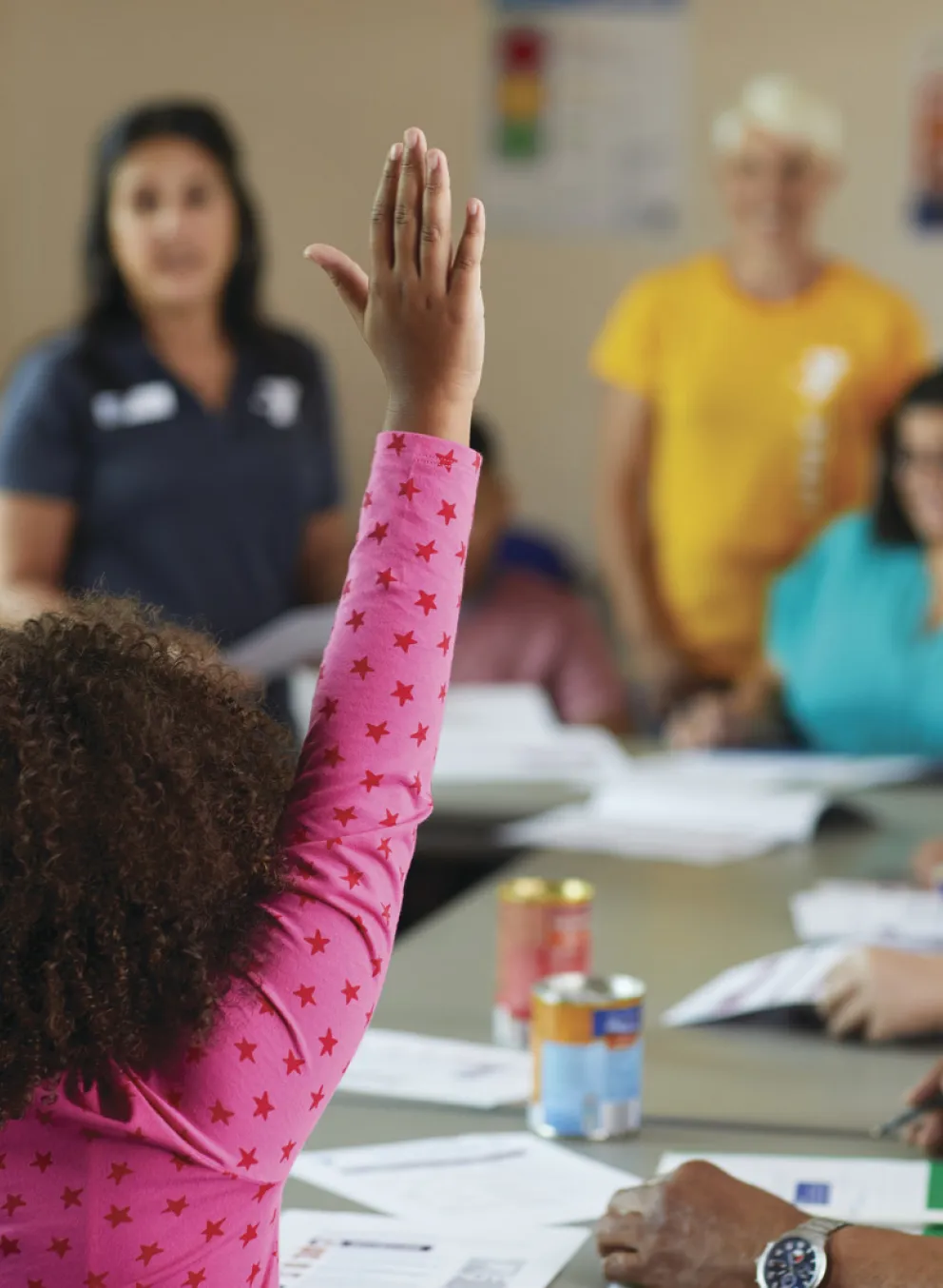 A child in a classroom raising their hand to ask a question.