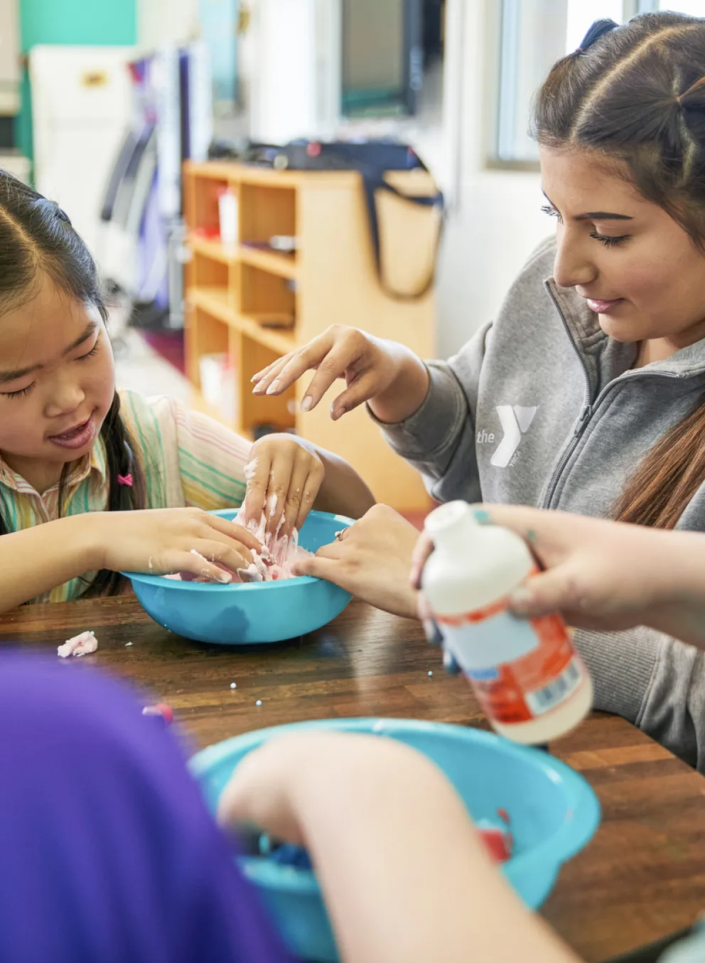 A group of children sit with a YMCA staff member doing a craft activity.