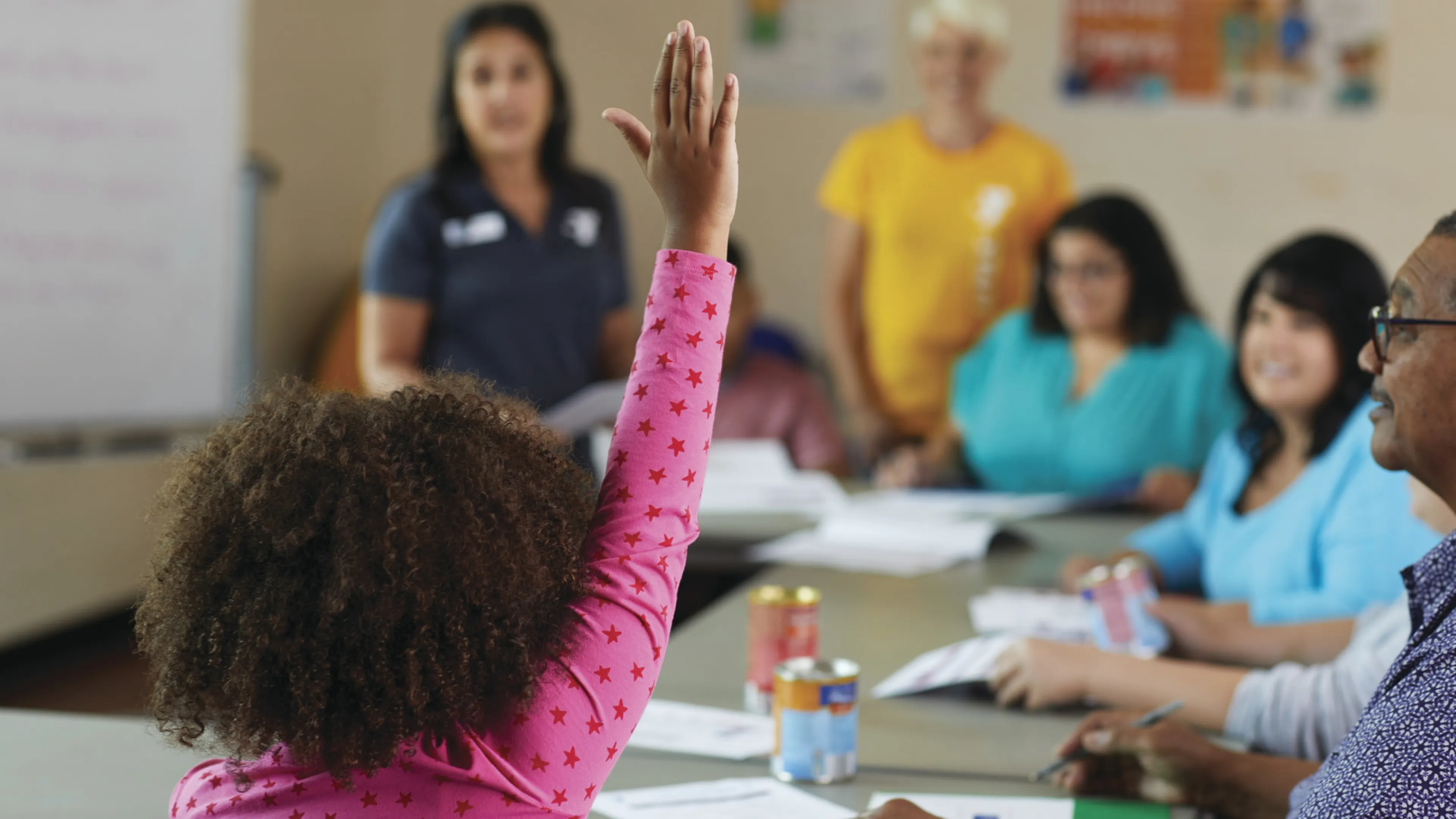 A child in a classroom raising their hand to ask a question.