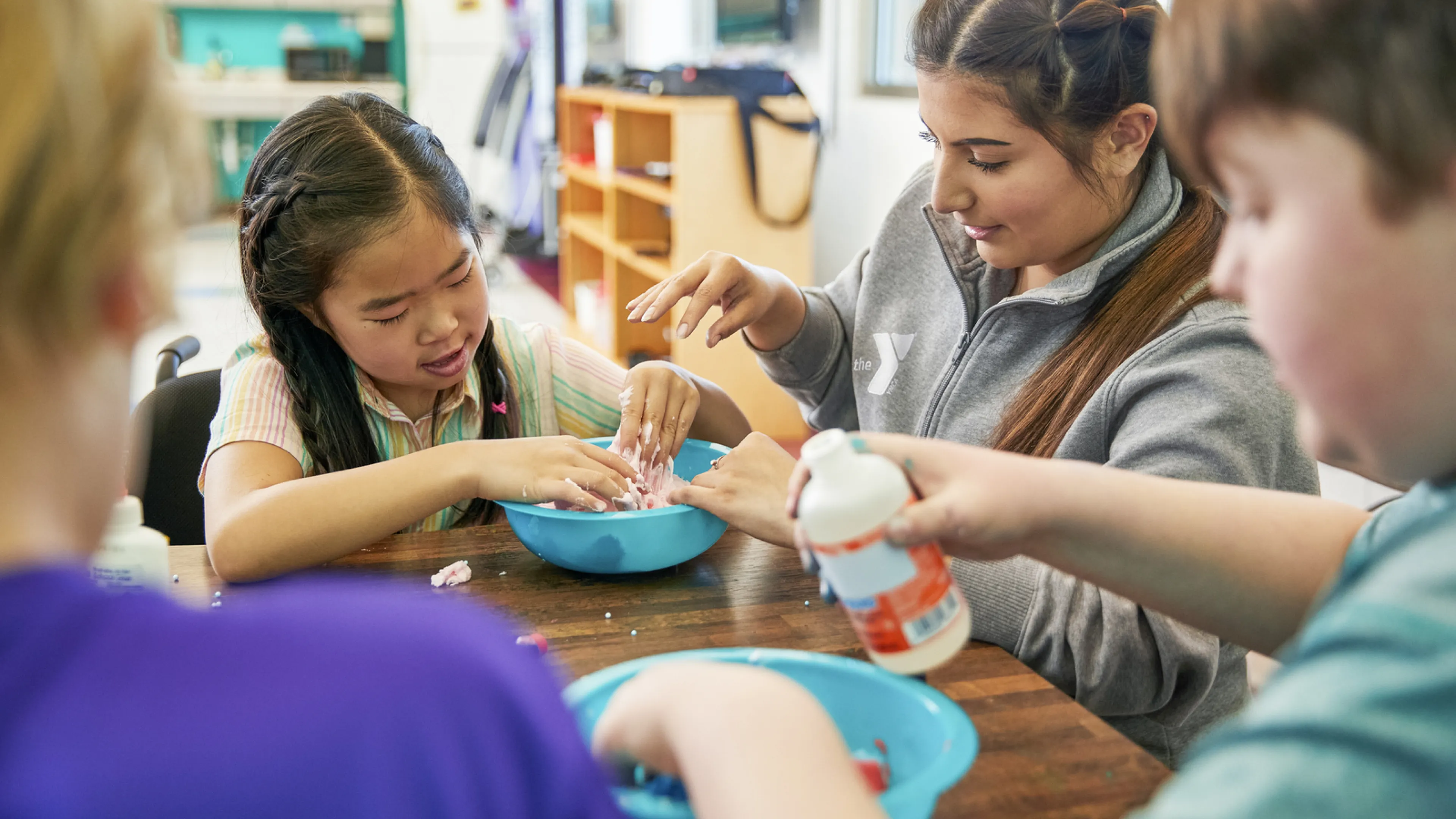 A group of children sit with a YMCA staff member doing a craft activity.